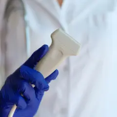 Dłoń w niebieskiej rękawiczce trzyma sondę do badania dopplerowskie.