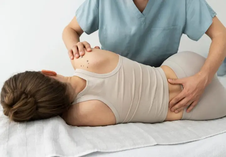 Fizjoterapeuta masuje odcinek lędźwiowy kręgosłupa pacjentki, pomagając w leczeniu dyskopatii lędźwiowej.