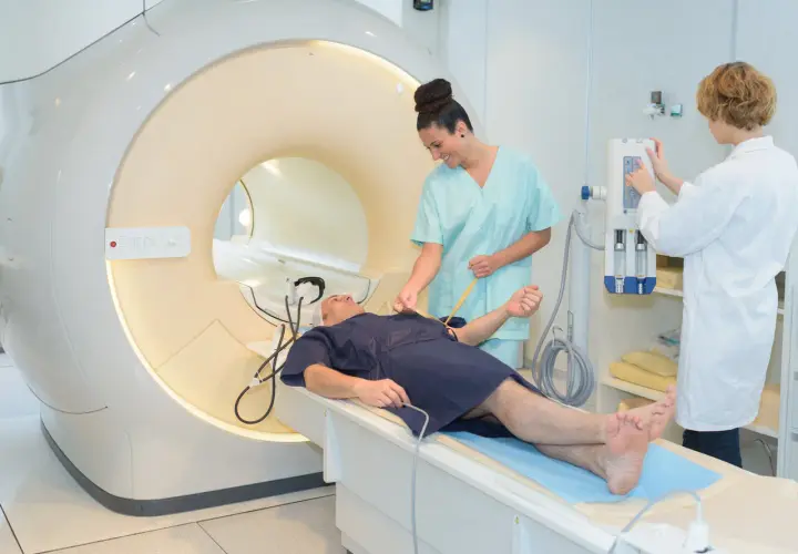 Pacjent leży na łóżku przed aparatem MRI, gdzie pielęgniarka przygotowuje go do badania. To właśnie mri co to za badanie?